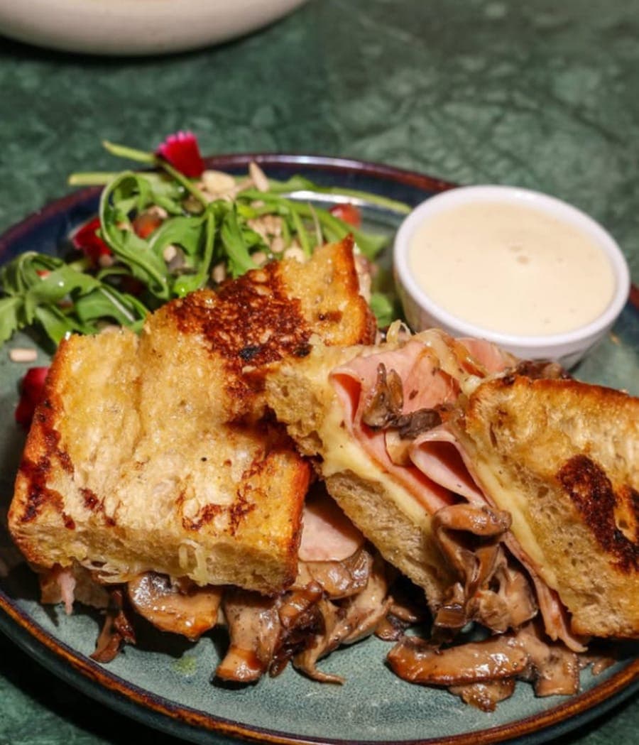 Sandwich grillé au jambon, fromage fondu et champignons avec salade de roquette